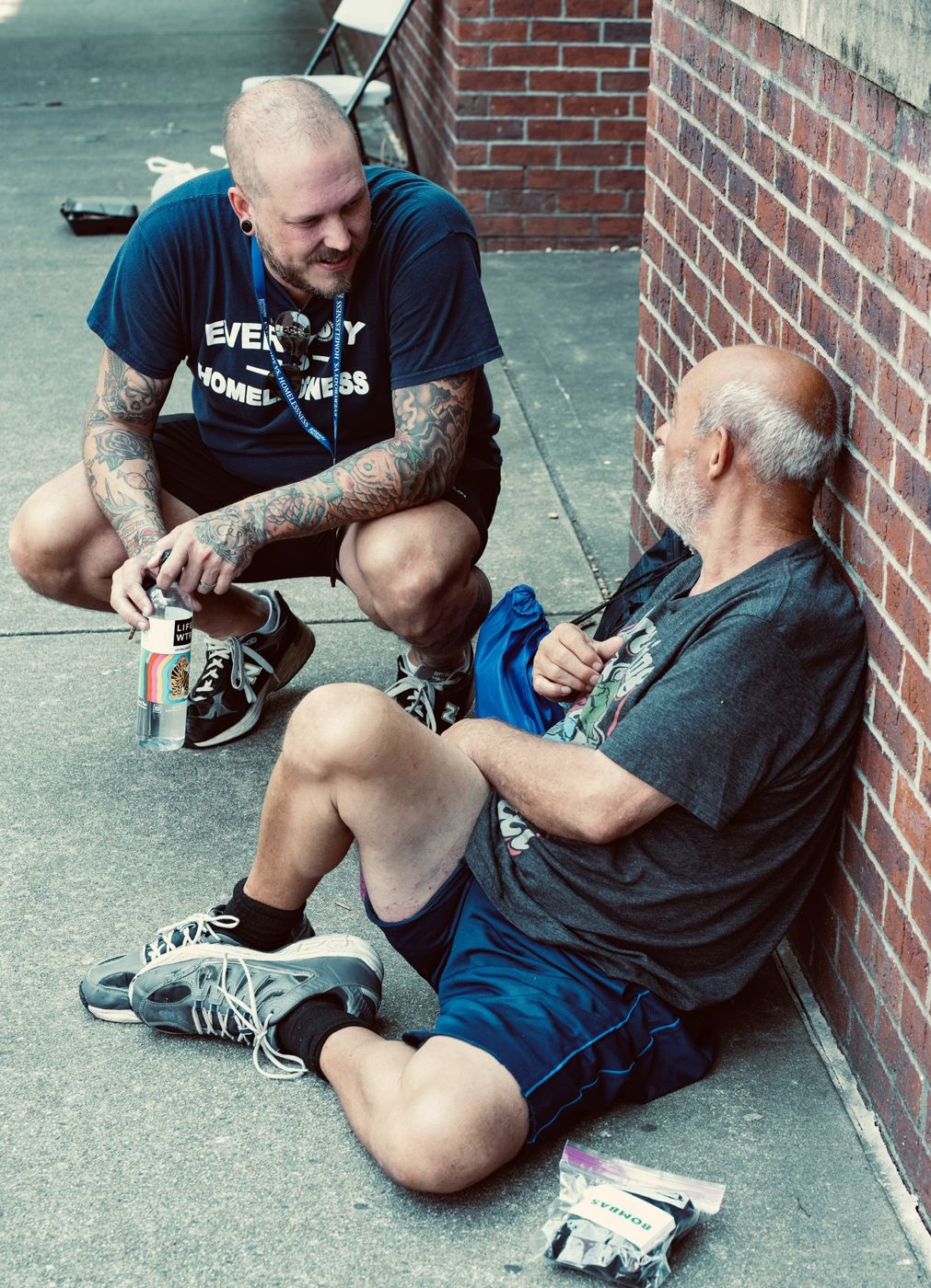 Drew kneeling to talk with a man sitting against a brick wall